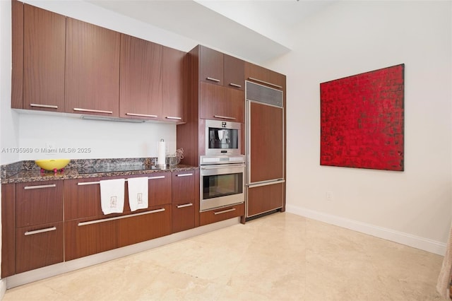 kitchen featuring baseboards, dark stone counters, paneled built in refrigerator, and modern cabinets