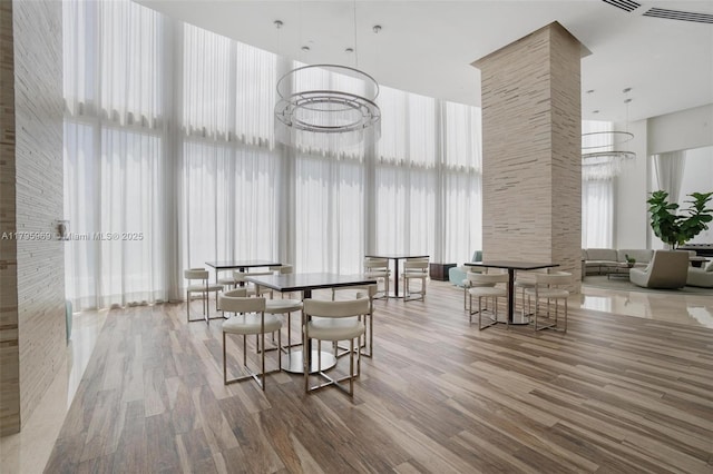 dining space featuring visible vents, decorative columns, wood finished floors, and a towering ceiling