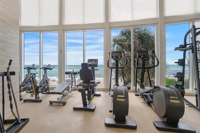 gym featuring floor to ceiling windows, a water view, a high ceiling, and a healthy amount of sunlight