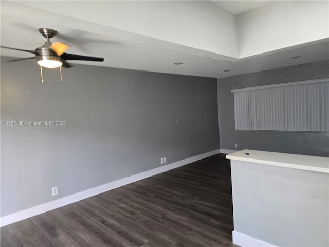 spare room featuring baseboards, a ceiling fan, and dark wood-style flooring
