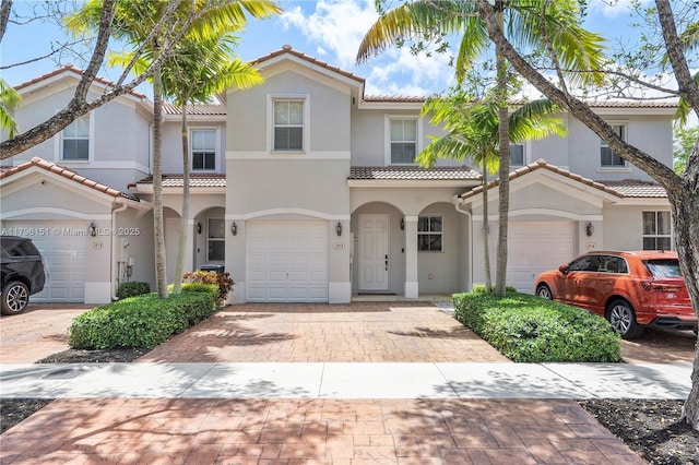 townhome / multi-family property with stucco siding, an attached garage, a tile roof, and decorative driveway
