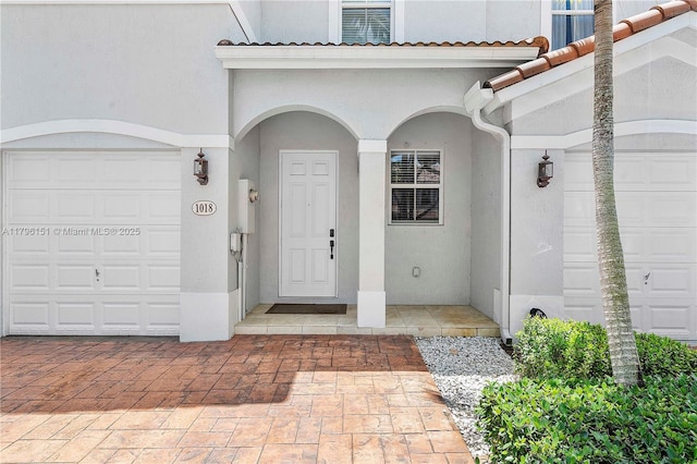 view of exterior entry with a garage and stucco siding