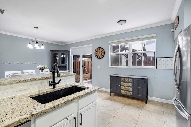 kitchen with an inviting chandelier, freestanding refrigerator, white cabinets, a sink, and hanging light fixtures
