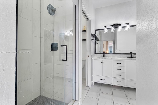bathroom with a textured wall, a sink, toilet, double vanity, and a stall shower
