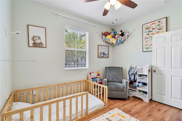 bedroom featuring a nursery area, a ceiling fan, and wood finished floors