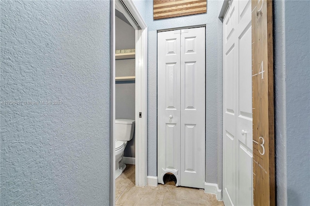 bathroom with toilet, a textured wall, tile patterned floors, and a closet