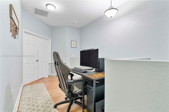 home office featuring visible vents, a textured wall, baseboards, and light wood-type flooring
