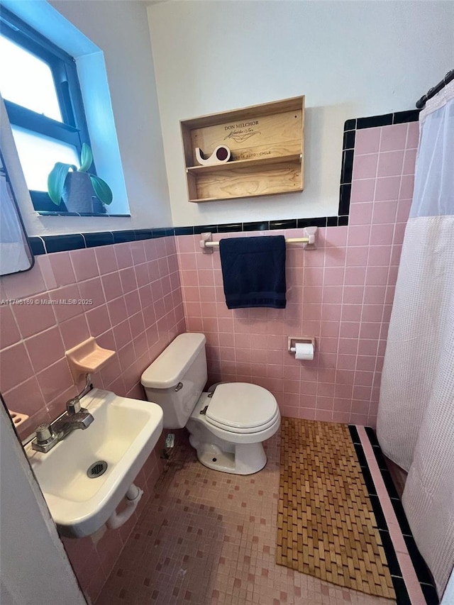 bathroom with tile walls, wainscoting, curtained shower, a sink, and toilet