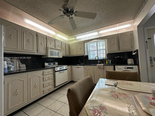 kitchen featuring a ceiling fan, dark countertops, white appliances, a sink, and light tile patterned floors