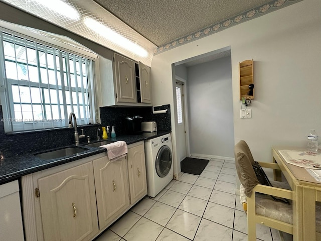 kitchen with backsplash, washer / clothes dryer, dark countertops, dishwasher, and a sink