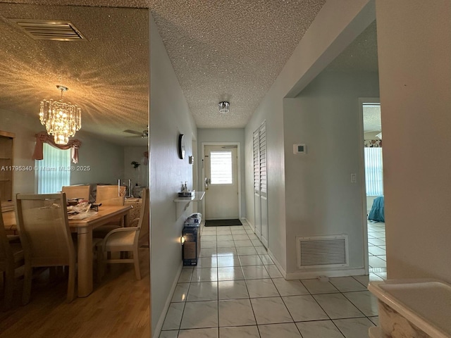 hallway featuring light tile patterned floors, a textured ceiling, visible vents, and an inviting chandelier