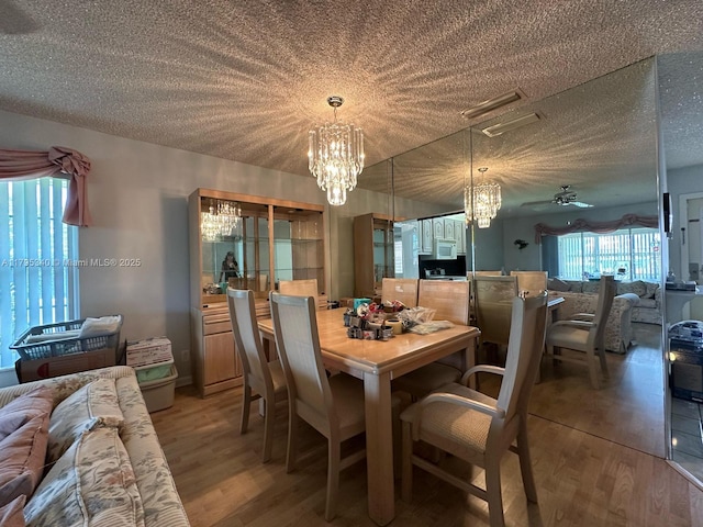 dining space featuring ceiling fan with notable chandelier, light wood finished floors, and a textured ceiling