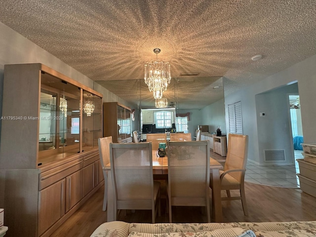 dining room featuring visible vents, a textured ceiling, wood finished floors, and a notable chandelier