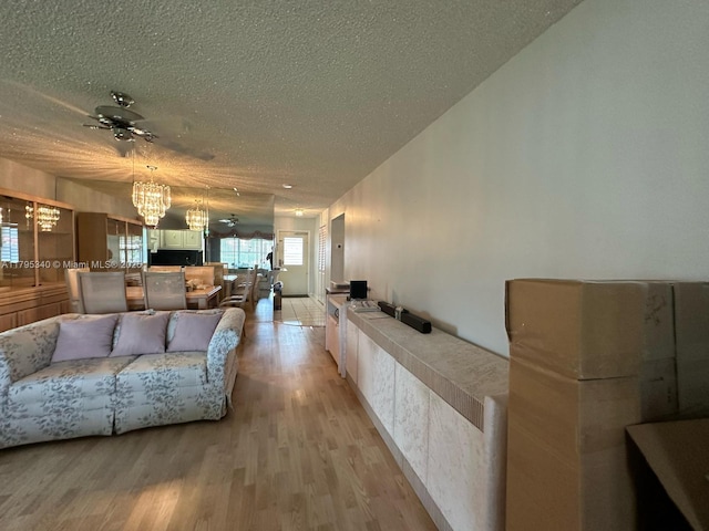 living area with a textured ceiling, light wood finished floors, and ceiling fan with notable chandelier