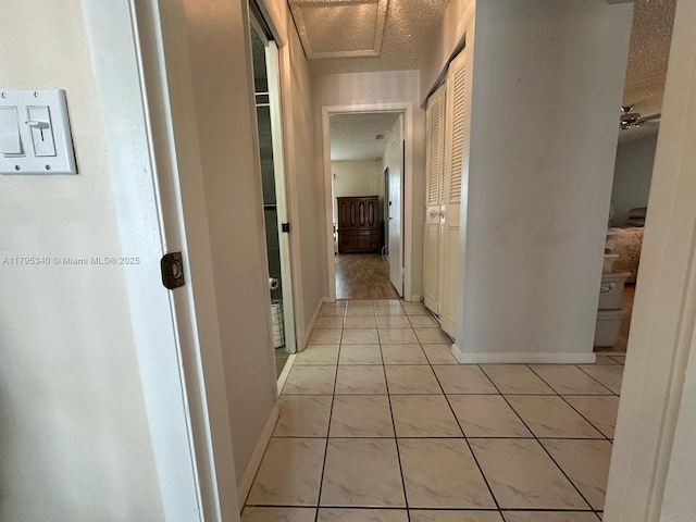 hall with baseboards, a textured ceiling, and light tile patterned flooring