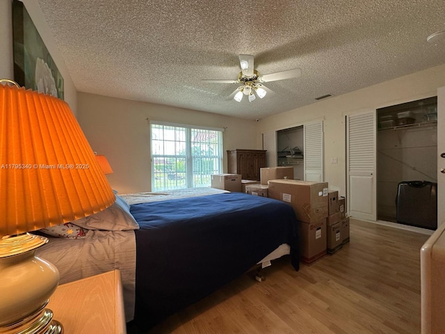bedroom featuring a ceiling fan, a textured ceiling, visible vents, and wood finished floors