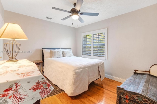 bedroom featuring baseboards, a ceiling fan, wood finished floors, and visible vents