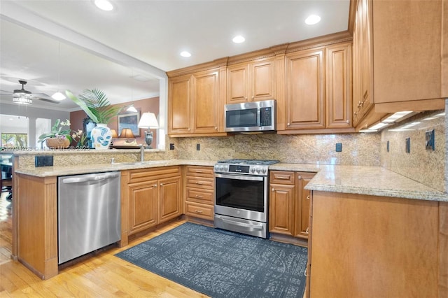 kitchen featuring backsplash, appliances with stainless steel finishes, a sink, light wood finished floors, and a peninsula
