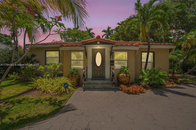 exterior entry at dusk with a tiled roof and stucco siding