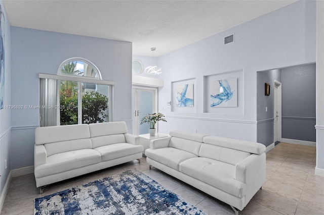living room featuring a textured ceiling, visible vents, tile patterned flooring, baseboards, and an inviting chandelier