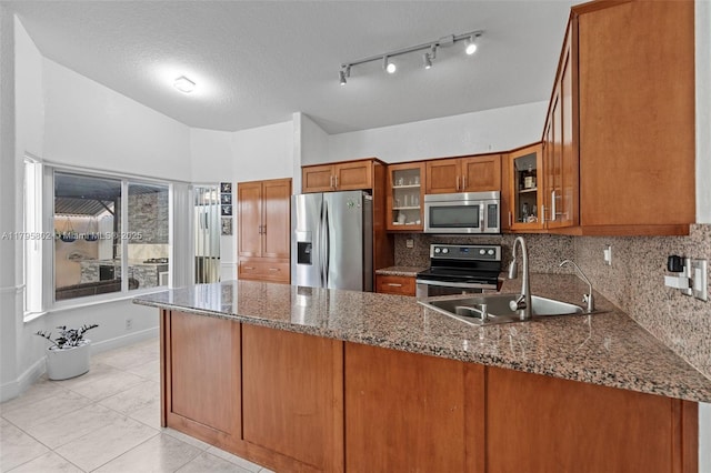 kitchen featuring brown cabinetry, appliances with stainless steel finishes, a sink, dark stone countertops, and a peninsula