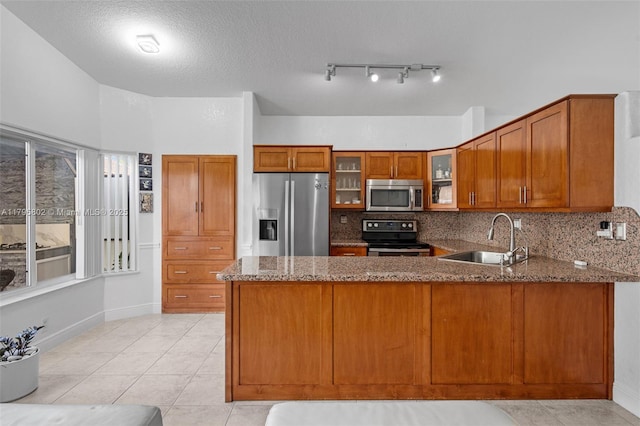 kitchen with a peninsula, brown cabinets, a sink, stone counters, and appliances with stainless steel finishes