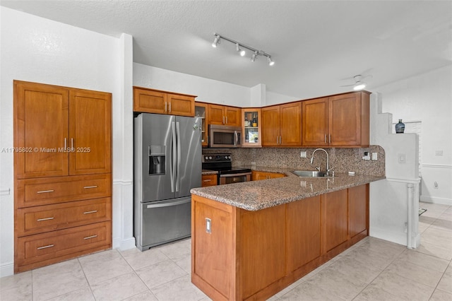 kitchen with appliances with stainless steel finishes, a sink, brown cabinetry, a peninsula, and stone counters