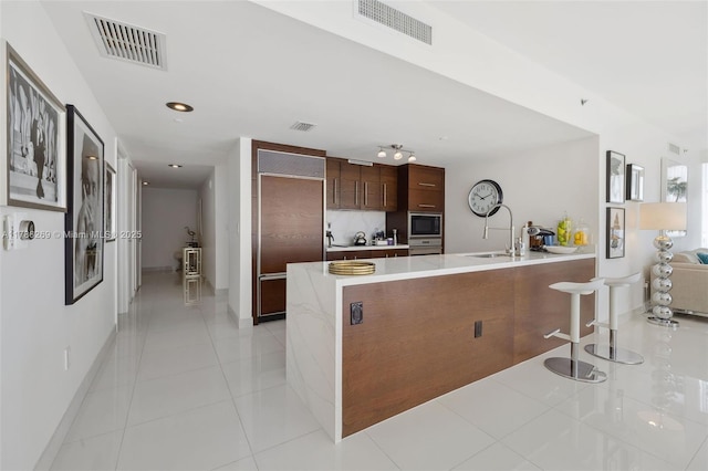 kitchen featuring built in appliances, a peninsula, visible vents, and a sink