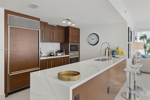 kitchen featuring visible vents, built in appliances, light stone countertops, modern cabinets, and a sink