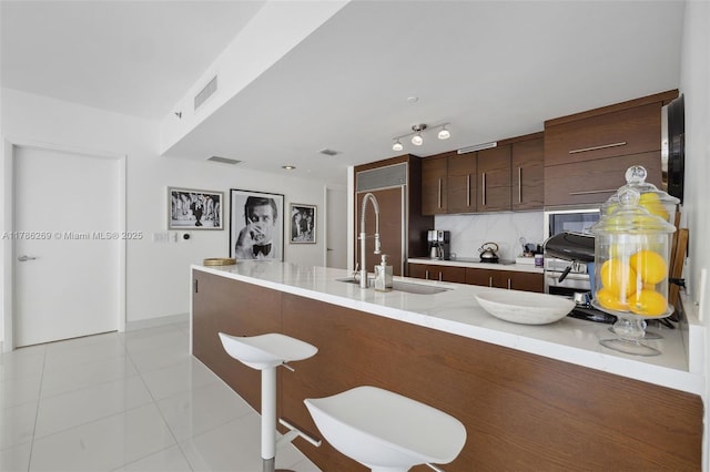 kitchen with light tile patterned flooring, dark brown cabinetry, a sink, a peninsula, and backsplash
