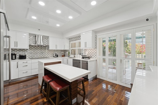 kitchen featuring wall chimney range hood, a sink, a breakfast bar area, a center island, and dark wood-type flooring