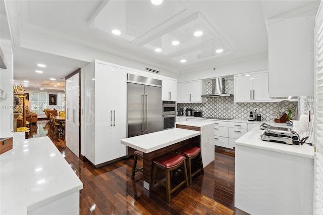 kitchen featuring wall chimney range hood, a center island, stainless steel appliances, recessed lighting, and dark wood-type flooring
