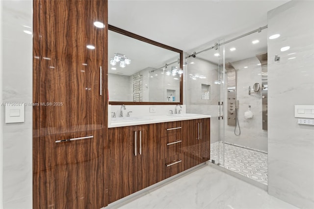 full bath with a sink, a marble finish shower, and double vanity