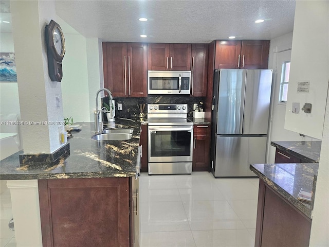 kitchen with dark brown cabinets, a sink, dark stone countertops, stainless steel appliances, and a peninsula