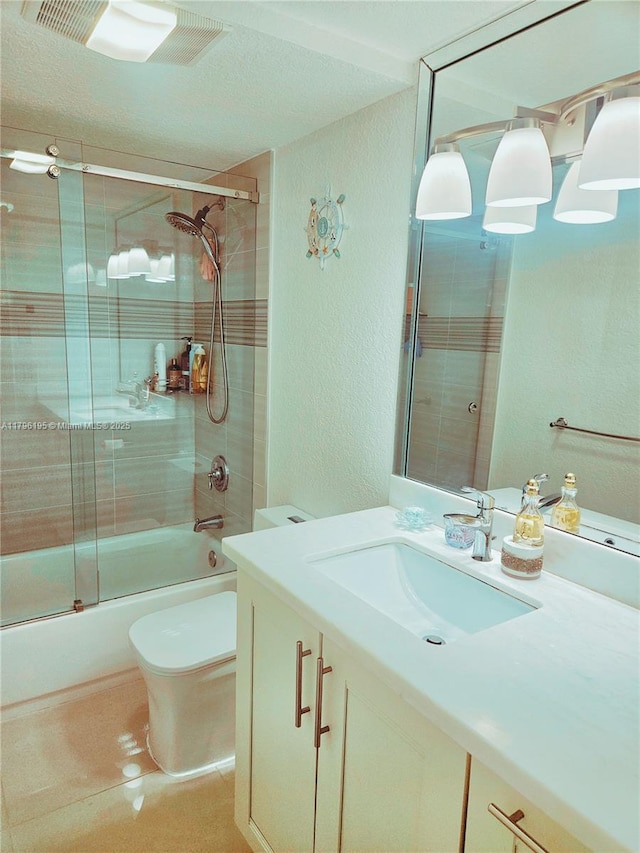 full bathroom featuring vanity, visible vents, a textured wall, toilet, and combined bath / shower with glass door