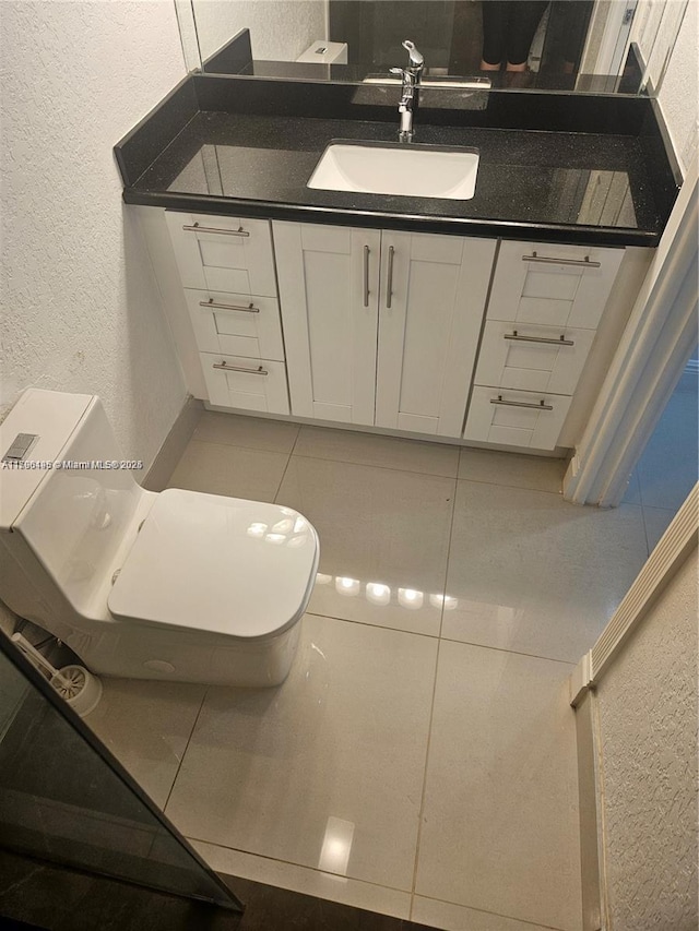 half bath featuring toilet, a textured wall, and vanity