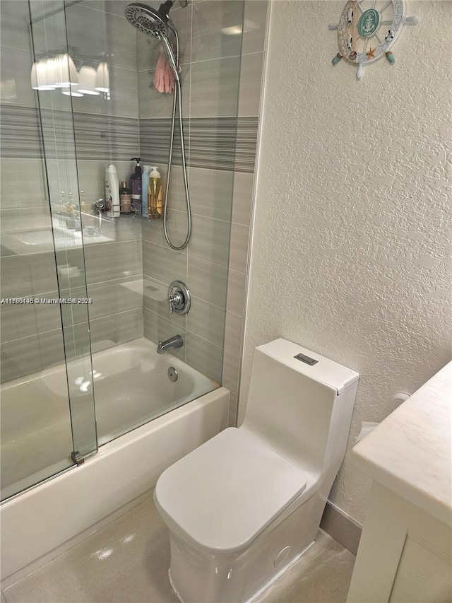 bathroom featuring a textured wall, toilet, and shower / bath combination with glass door