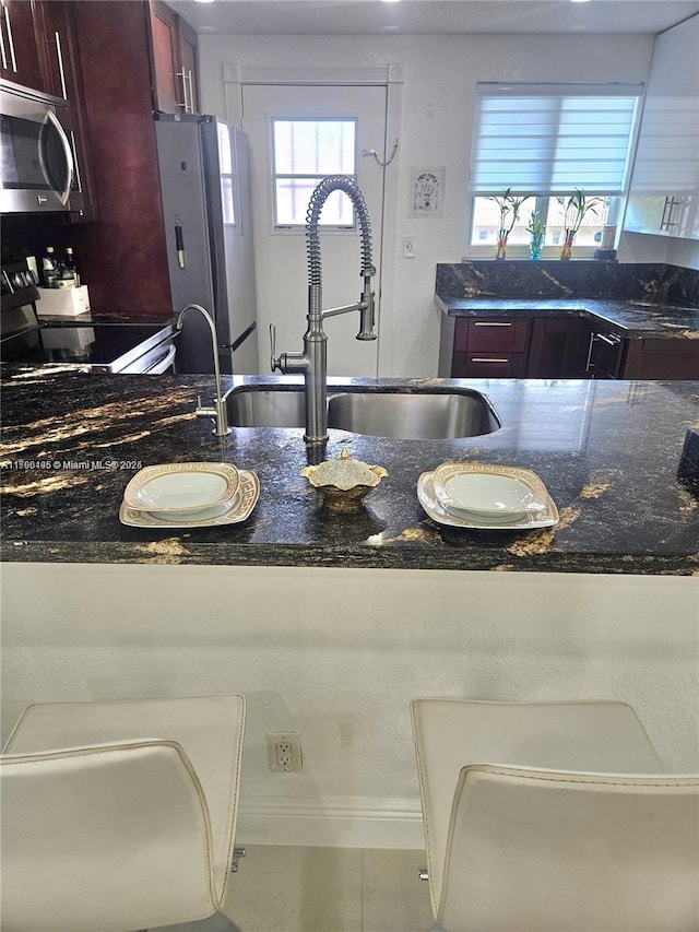 kitchen with reddish brown cabinets, a sink, dark stone countertops, and appliances with stainless steel finishes