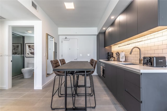 kitchen featuring visible vents, light countertops, tasteful backsplash, a sink, and light tile patterned floors