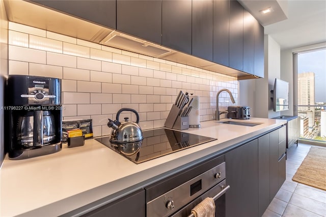 kitchen featuring decorative backsplash, stainless steel oven, black electric stovetop, a sink, and light tile patterned floors