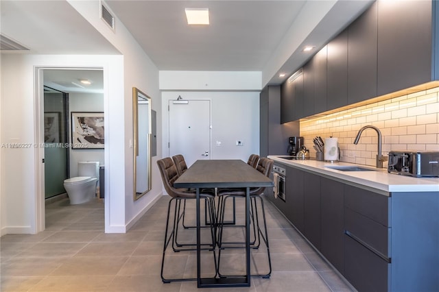 kitchen featuring visible vents, light countertops, tasteful backsplash, a sink, and light tile patterned floors