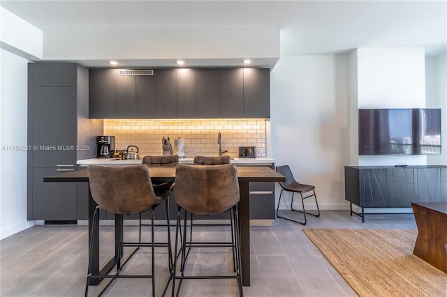 kitchen featuring visible vents, modern cabinets, tasteful backsplash, a breakfast bar, and light tile patterned flooring