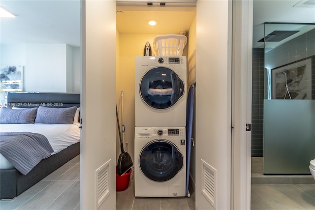 clothes washing area with visible vents, stacked washer and clothes dryer, and tile patterned flooring