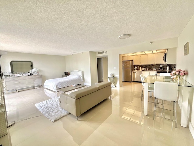 bedroom featuring visible vents, freestanding refrigerator, a textured ceiling, and light tile patterned flooring