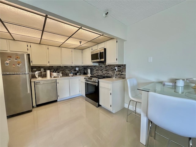 kitchen featuring light countertops, white cabinets, tasteful backsplash, light tile patterned floors, and stainless steel appliances