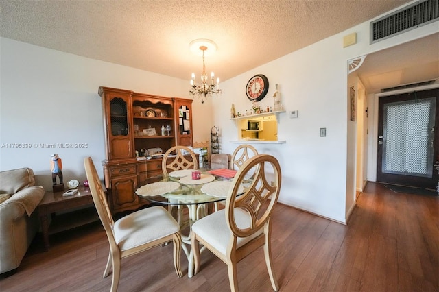 dining room with a textured ceiling, visible vents, wood finished floors, and an inviting chandelier
