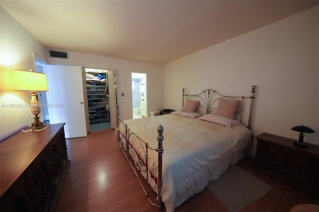 bedroom featuring visible vents, a closet, wood finished floors, a spacious closet, and ensuite bath