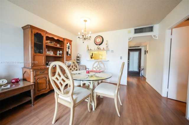 dining area featuring visible vents, a textured ceiling, wood finished floors, and a chandelier