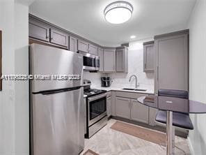 kitchen featuring light countertops, stainless steel appliances, gray cabinetry, and a sink