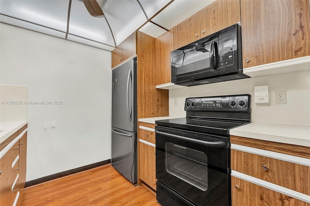 kitchen with light countertops, light wood-style flooring, brown cabinets, and black appliances